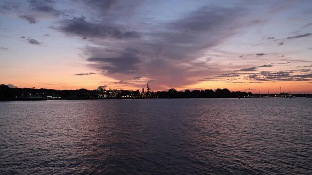 Beautiful summer sunrise over the IJ waterfront and port area in Amsterdam, Netherlands. Colorful morning sky with dramatic clouds and warm sunlight over the water. Scenic real-time view.