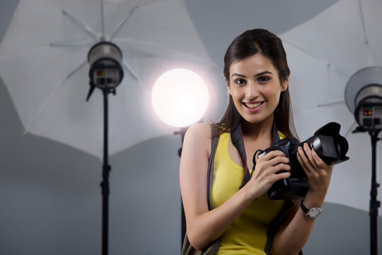 Portrait of beautiful young photographer holding camera in her studio 