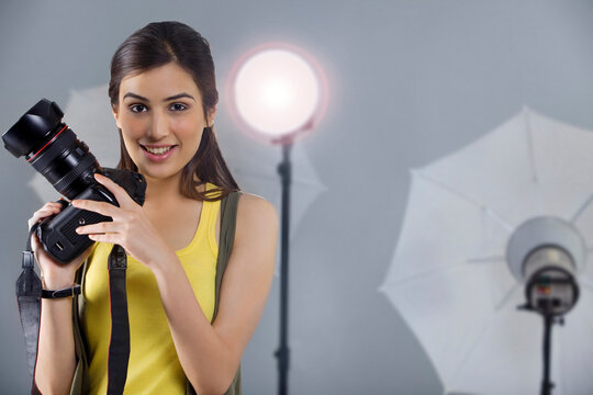 Portrait of smiling female photographer in front of spotlight in studio shot 