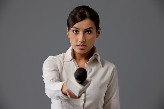 Close-up of serious reporter holding out microphone 