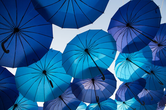 Shades of blue umbrellas create a dramatic overhead pattern, outdoor decorative installation, creative festival background, summer travel theme.