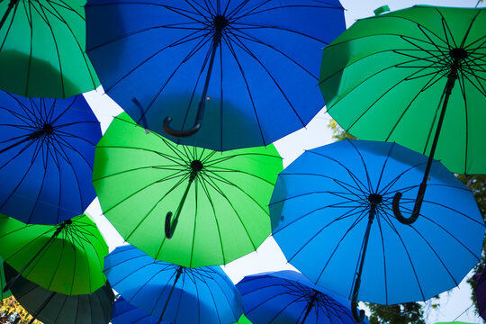 Blue and green umbrellas create a bold geometric canopy in the open air, vibrant outdoor festival decoration.