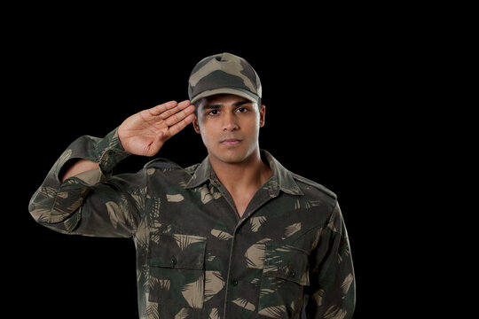 Portrait of male Indian soldier saluting over black background 