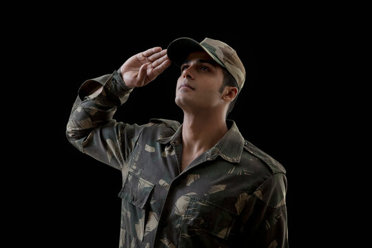 Soldier saluting while looking up against black background 