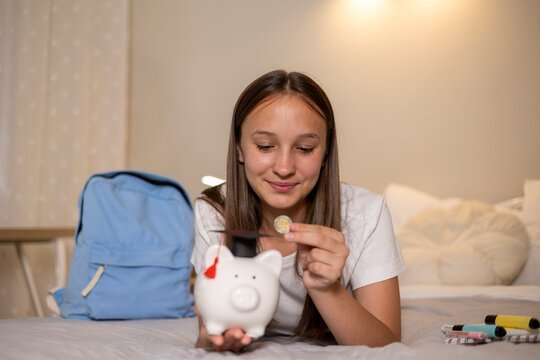 Teenage girl saving money for education and future studies using a piggy bank, symbolizing financial planning and educational goals.