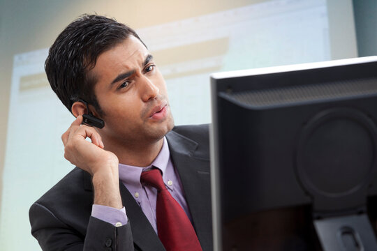 Smart male executive looking at computer while conversing on call 