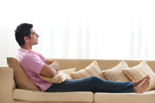 Full length of handsome young man day dreaming on sofa 
