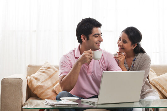 Loving young man looking at woman while holding coffee cup with laptop 