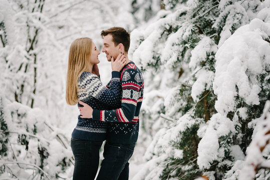 Loving couple looking tenderly at each other, hugging in winter forest among snowy spruce trees. Romantic moments of happiness. Closeup.