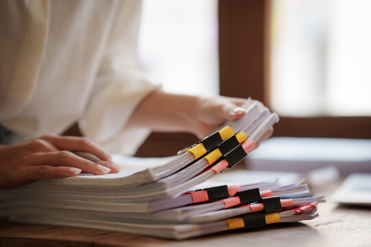 Business professional reviewing documents and paperwork at a desk with laptop, smartphone, calculator, and organized files in a modern office.