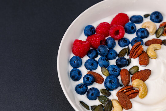 Close up of healthy yogurt bowl with fresh blueberries, raspberries, nuts and seeds, copy space on dark background, health food concept