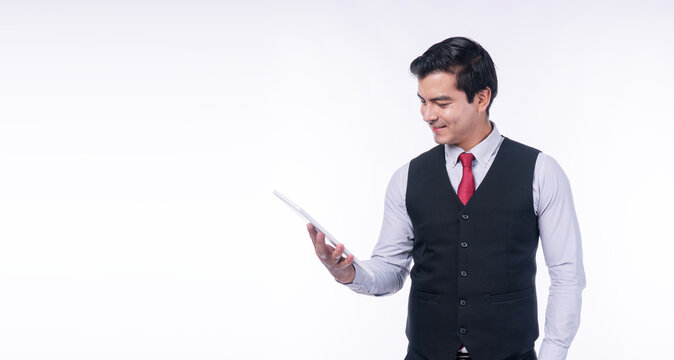 Confident young handsome businessman in black vest and red tie smiling while using a digital tablet isolated on white background with copy space. Corporate communication and modern business concept.