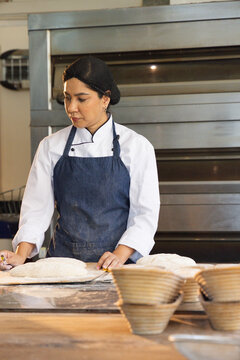 Mid adult African American woman in chef coat shaping dough at bakery bench with bannetons