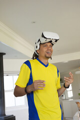 Fototapeta premium Man wearing yellow blue sports shirt and VR headset on forehead, gesturing in open living room