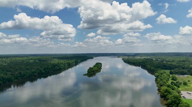 Aerial drone shot flying over Potomac river with a wooded island at Algonkian Regional Park, Sterling VA. Lush green summer forests and blue cloudy skies reflect in the tranquil water.