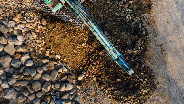 Aerial view of an excavator working on a rocky construction site with piles of stones and soil in Karanglewas, Central Java, Indonesia.