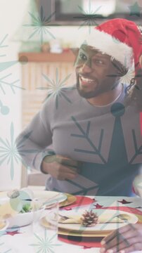 Animation of snow falling over smiling family with santa hats having dinner