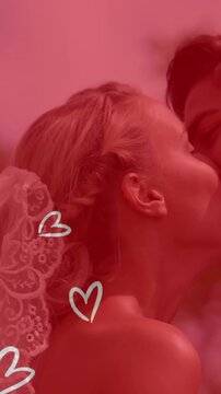 Animation of white hearts over caucasian couple wearing wedding clothes and kissing