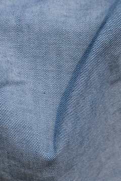 Vertical image of Crumpled light blue denim fabric macro texture with visible folds and woven fibers. Versatile textile background for fashion, apparel, material, and design concepts