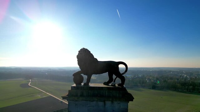 Napoleon Battlefield, Waterloo, Walloon Brabant, Belgium, March 4th, 2025, A majestic lion statue stands guard proudly, bathed in golden sunlight, overlooking a serene field and beautiful sky