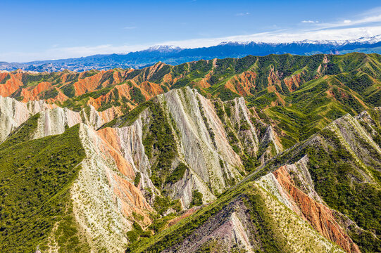Aerial view of sunlit green and ochre ridges in Xinjiang, China, showing rugged mountain terrain, deep valleys, and natural erosion for travel and geography projects.