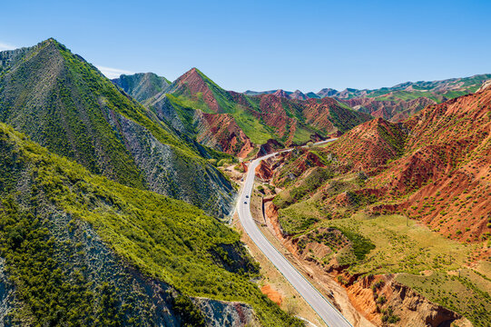 Winding asphalt road through eroded green hills and dry ravines in Xinjiang, China, offering travel, infrastructure, and rural landscape appeal.