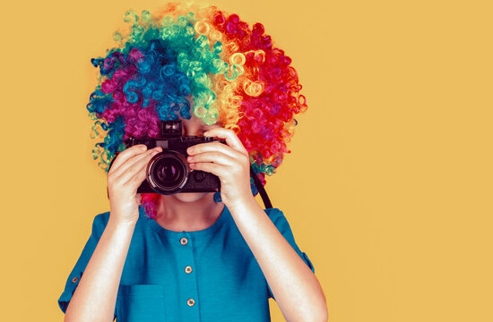 Little boy on a taking a photo using a vintage camera. Smiling little boy in clown wig