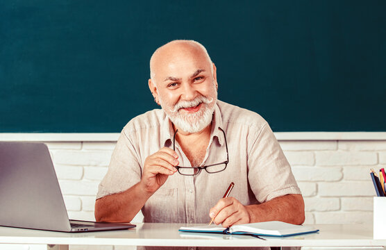 Teachers on green board. Portrait male teacher in classroom. Male teacher with laptop in class sits at the table