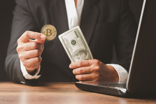 Person Holding Bitcoin Coin and US Dollar Cash Beside Laptop