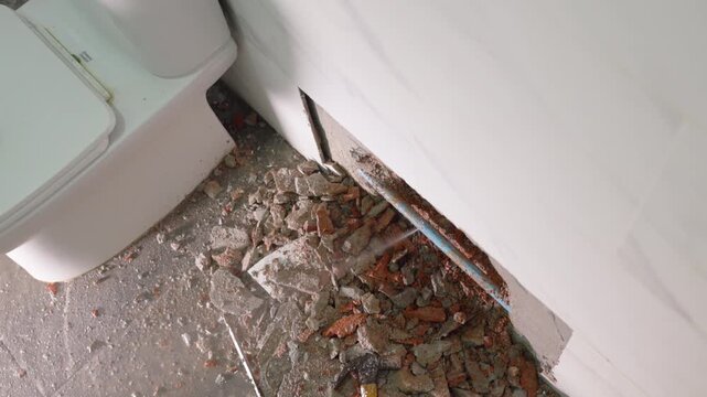 Exposed plumbing pipe inside a cracked wall reveals hidden home maintenance problems, water leakage, moisture damage, corrosion, renovation work, and the need for professional repair.