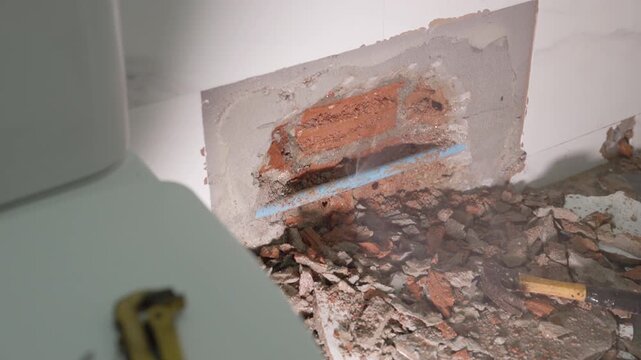 Exposed plumbing pipe inside a cracked wall reveals hidden home maintenance problems, water leakage, moisture damage, corrosion, renovation work, and the need for professional repair.