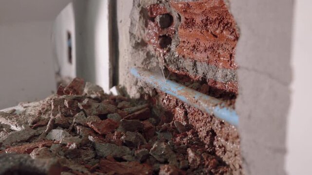 Exposed plumbing pipe inside a cracked wall reveals hidden home maintenance problems, water leakage, moisture damage, corrosion, renovation work, and the need for professional repair.