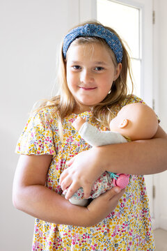 Proud chubby smiling little blond girl in summer dress cradling her baby doll tenderly, Quebec City Quebec, Canada