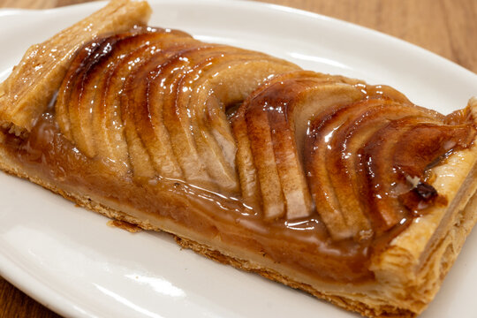 Normandy artisan bakery apple tart with thinly sliced, caramelized apples on buttery puff pastry with glossy glaze; sweet, French breakfast in bakery