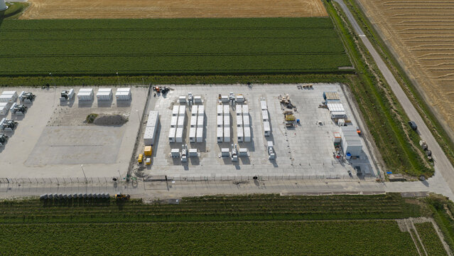 Aerial view of a battery energy storage system with rows of white containers on a concrete pad surrounded by agricultural fields in Dronten, Flevoland, Netherlands.