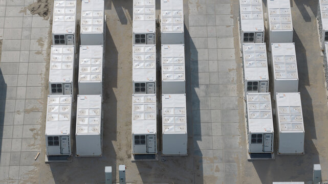 Aerial view of a battery energy storage system with rows of white shipping containers arranged on a concrete pad in Dronten, Flevoland, Netherlands.