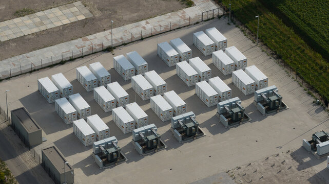 Aerial view of a battery energy storage system featuring rows of white shipping containers and electrical transformers in an industrial facility in Dronten, Flevoland, Netherlands.