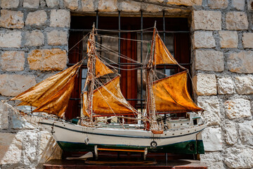 Close-up of a white sailing ship model with orange sails displayed on a rustic stone wall © Liana