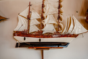 Close-up of a black and white model sailing ship with white sails on a white wall © Liana