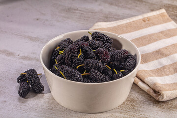 Fresh black mulberries in white ceramic bowl on textured surface with striped cloth © Andrei Starostin