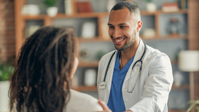 Smiling Male Doctor With Stethoscope Shaking Hands With Female Patient In Office, Displaying Trust And Professionalism In A Welcoming Clinic Setting. Healthcare Concept.