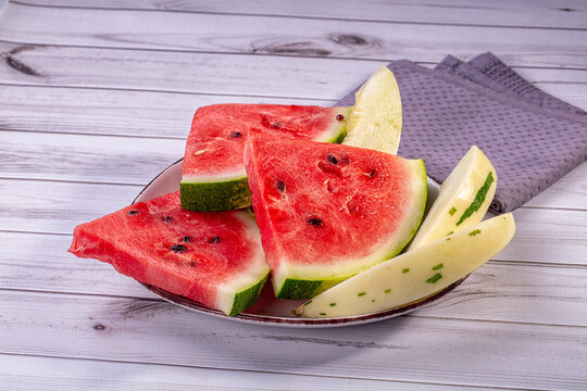 Sliced watermelon and melon on plate over white wooden table