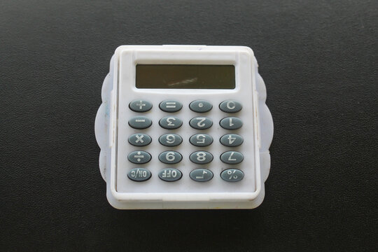 white toy mini pocket calculator with gray buttons, isolated on textured black background