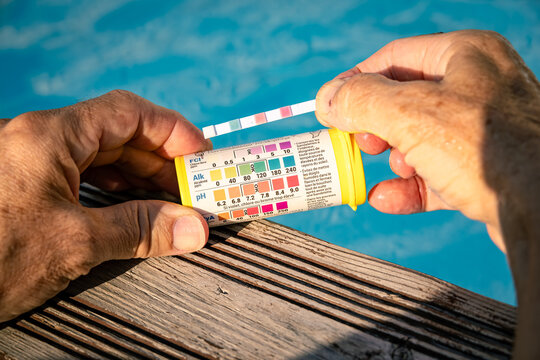 Hand testing swimming pool water quality with a test strip during routine home pool maintenance, checking pH and chlorine levels for safe and clean water on a sunny summer day.