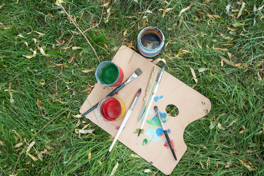 Artist palette with paintbrushes and paint lying down on the grass, top view with copy space