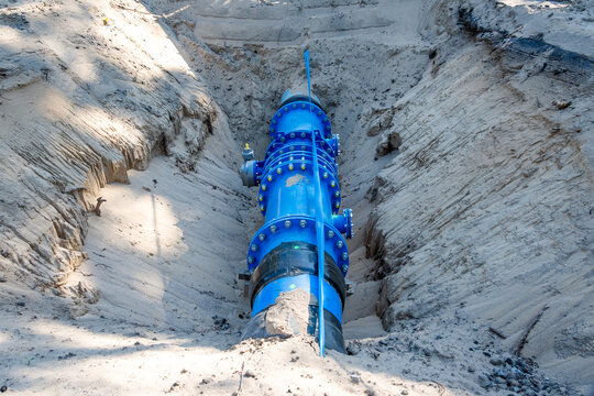 Eine in einem tiefen Graben im Wald freigelegte Wasserleitung aus blauem Kunststoff und Metall verdeutlicht den Ausbau der kritischen Infrastruktur und eine moderne Rohrleitungsverlegung.