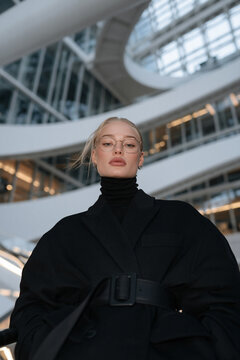 futuristic portrait of stylish person in modern architectural interior, elegant blonde model in black turtleneck against curved white architecture, sophisticated portrait with futuristic architecture