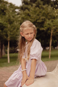 A blonde girl with long hair is sitting on a bench in the park.