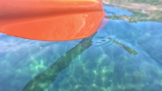 Kayak paddle turquoise water close up of an orange oar moving through clear ocean on a sunny day