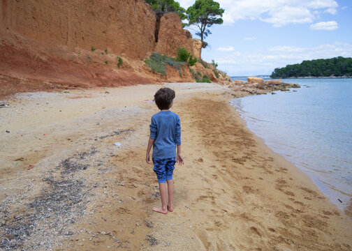 Little boy standing on a unique golden sand beach with reddish clay cliffs on Vrgada island, Croati